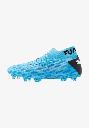 Taco de fútbol azul con parte superior texturizada, cuello tipo calcetín y detalles en negro. Cuenta con tacos translúcidos para mayor agarre en superficies de césped.