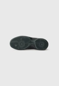 Schwarze Sportschuhsohle aus strukturiertem Gummi mit kreisförmigen Grip-Mustern und einem Nike-Logo. Aerodynamisches, geschwungenes Design.