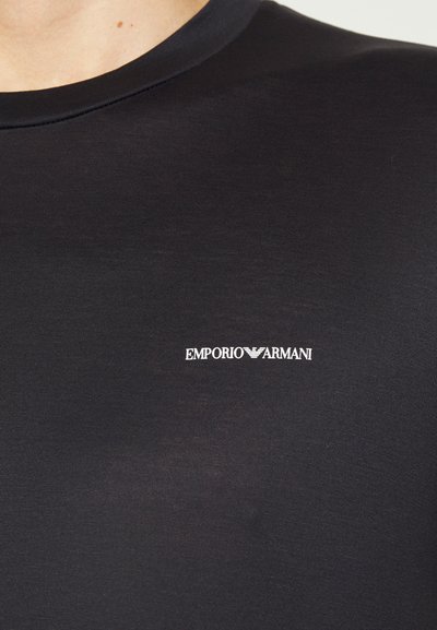 Juodas prigludęs marškinėliai, pagaminti iš lygaus audinio, su apvaliu iškirpimu ir baltu "EMPORIO ARMANI" logotipu krūtinėje.
