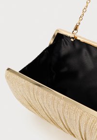 Clutchveske med gullglitter og teksturert bølgemønster, sort stoffinnside og tilhørende gullkjede som henger åpen.