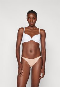 Soutien-gorge blanc à bordure en dentelle, avec des bonnets moulés, associé à un bas de bikini nude lisse. Bretelles ajustables et design minimaliste.
