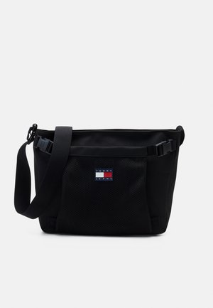 Černá crossbody taška s nastavitelným popruhem, přední síťovanou kapsou a logem Tommy Jeans uprostřed kapsy.