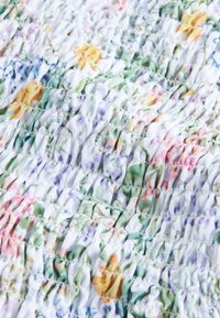 Materiál s kvetinovým vzorom na bielom podklade, ktorého povrch je nazbieraný do záhybov. Farby zahŕňajú ružovú, žltú, zelenú a fialovú v opakujúcom sa dizajne.