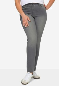 Jean gris slim fit avec une texture de tissu lisse, doté de cinq poches et de détails de couture subtils, associés à des baskets blanches.