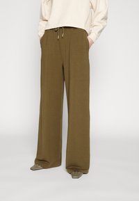 Olivgrön vida sweatpants med dragsko i midjan och sidofickor. Mjukt tyg med en slät yta, i kombination med snobbiga tåskor.