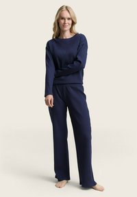 Marineblauw geribd loungewear-set bestaande uit een top met lange mouwen en bijpassende broeken met een relaxte pasvorm. Zachte textuur en lichtgewicht stof.