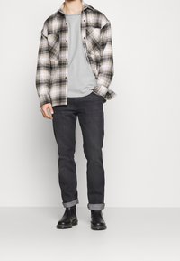 Karierte Flanellshirt in Schwarz, Weiß und Beige, über einem grauen T-Shirt getragen. Dunkle Jeans, hochgekrempelte Säume und schwarze Leder-Ankle-Boots.