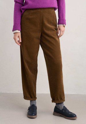 Pantaloni in corduroy marroni con un design a gamba larga e tessuto texturizzato. Abbinati a scarpe scure e calze grigie, con un pullover viola.