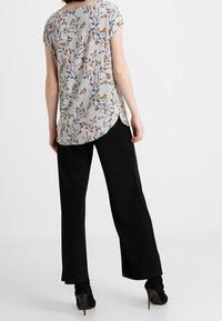 Blusa gris fluida con estampado floral, con mangas cortas y dobladillo curvado, combinada con pantalones anchos negros y tacones altos negros.