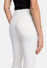 Weiße hochgeschnittene Jeans mit glatter Textur, die zwei Gesäßtaschen und dezente Nähedetails entlang der Nähte aufweisen.