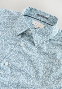 Világoskék ing paisley mintával. Simább tapintású anyagból készült, gombos gallérral és fehér gombokkal.