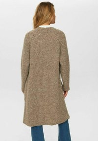 Lång, stickad kofta i beige med en strukturerad mönstring, med raglanärmar, rund halsringning och en något rundad fåll.