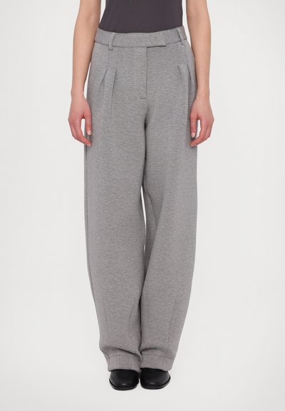 Grau-weitbeinige Hose aus weichem Stoff, mit Vorderfalten und einem bequemen elastischen Bund. Kombiniert mit schwarzem Schuhwerk.