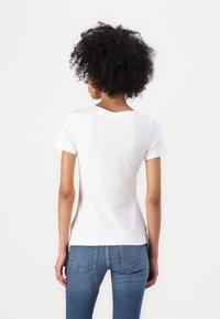White cotton t-shirt with short sleeves and a round neckline, worn with fitted blue jeans, showing a smooth texture and a simple design.