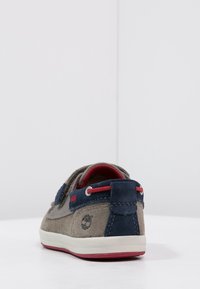 Zapatos de ante en gris y azul marino, con un acento en rojo, punta redonda, suela blanca y logotipo en el talón. Textura suave con cierre de cordones.