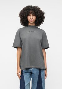 Šedé krátke tričko s oversized strihom a vysokým golierom, na ktorom je vytlačené logo "KARL LAGERFELD JEANS" na hrudi. Mäkko bavlnené materiály.