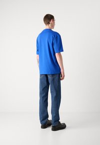 Blå kortermet t-skjorte med avslappet passform kombinert med rette blå denimjeans og svarte sko, sett bakfra.