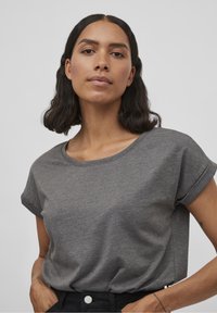 Grå kortærmet T-shirt i blødt bomuldsstof, med rund halsudskæring og opsmøgte ærmer, båret med højhalsede sorte bukser.