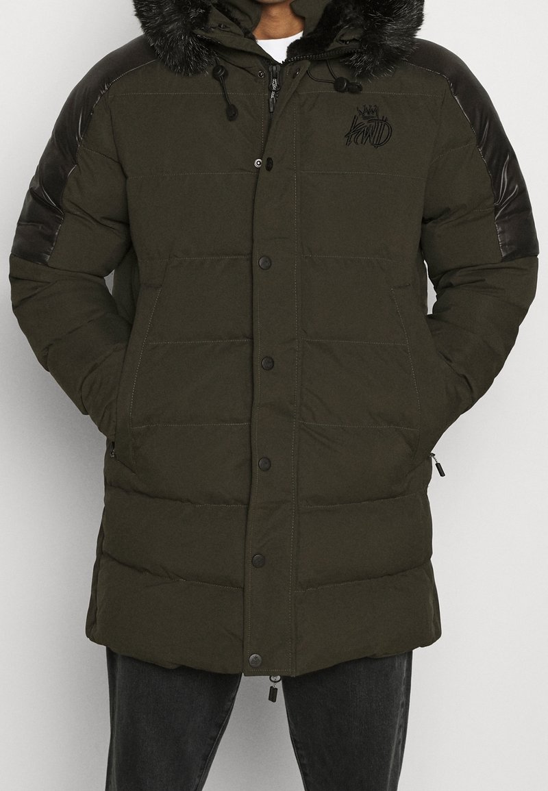 Chaqueta acolchada verde oliva con capucha de piel sintética desmontable, detalles en cuero negro en los hombros y cierre frontal con botones; textura acolchada.