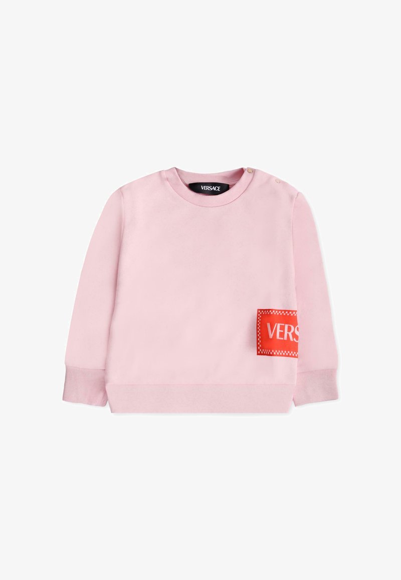 Felpa rosa chiaro con maniche lunghe, collo a giro, e una toppa rossa con la scritta "VERS" sul davanti. Dotata di bottoni a pressione sulle spalle.