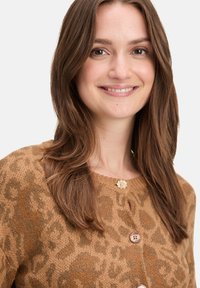 Cardigan imprimé léopard marron en tricot texturé, avec un col rond, trois boutons et une embellissance florale au col.