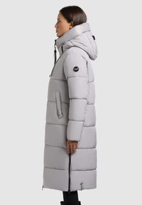 Vadderad gr�å parka med hög krage, huva, framdragkedja och sidofickor; har en logotypapplikation på ärmen och en knälång design.