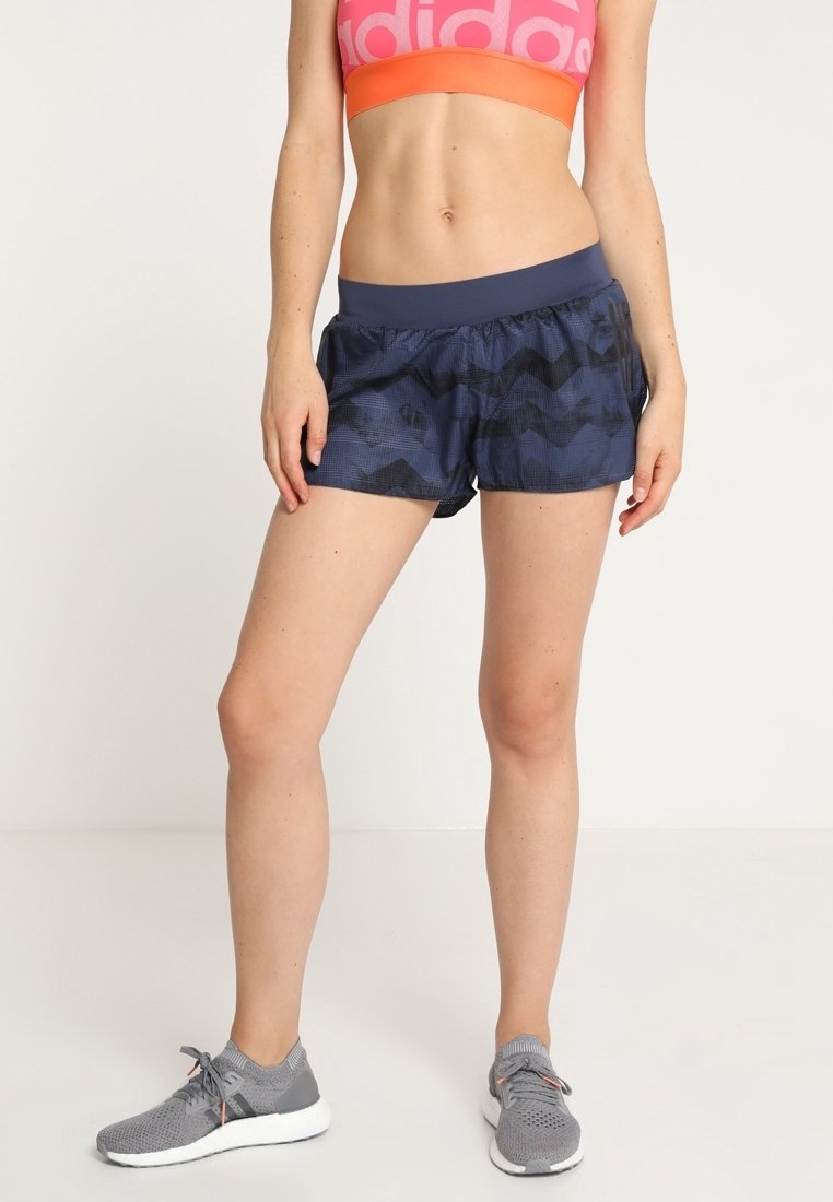 Shorts deportivos azul marino con un patrón de chevrones, cinturilla elástica y tejido ligero, combinados con zapatillas de correr grises.