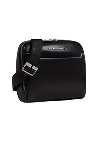 Bolso de cuero negro con forma rectangular, costuras de acento azul, herrajes plateados y una correa negra desmontable. Cierre superior con cremallera.