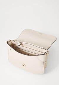 Beige læder crossover taske med klap, guld hardware, indvendig lomme med lynlås og flere rum. Tekstureret overflade med en glat finish.