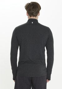 Langarm, donkergrijze sporttop met hoge kraag, gladde textuur en minimalistisch ontwerp. Bevat een klein logo op de nek.