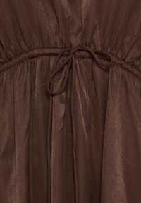 Brun kjole i stof med en indsnævret talje bundet med en sløjfe lavet af en tynd matchende snor.
