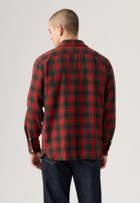 Rood en groen geruite shirt met lange mouwen, een knoopsluiting aan de kraag en zij-splitten. Van katoen met een zachte textuur.