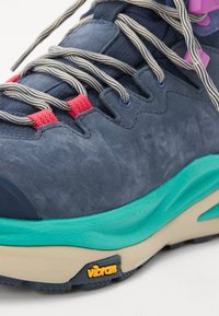 Footwear featuring a dark blue suede upper with teal midsole, contrasting red and purple accents, and Vibram branding on the sole.