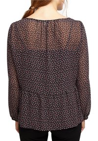 Blusa nera floreale con maniche lunghe trasparenti, dotata di scollatura rotonda, sottili motivi floreali rossi e bianchi, e orlo a peplo.