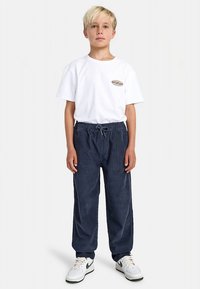 Bela bombažna majica s kratkimi rokavi, na sprednji strani je našitek z logotipom. Temno modre hlače z elastiko in vrvico za zavezovanje, ravnega kroja, gladke teksture, s stranskimi šivi.