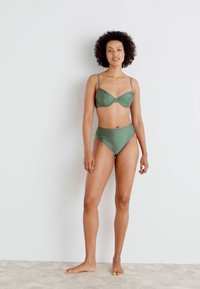 Žalias dviejų dalių bikini komplektas, kuriame yra liemenėlė su laidais ir reguliuojamomis petnešomis, kartu su aukšto juosmens bikini apatiniais. Sklandus paviršius.