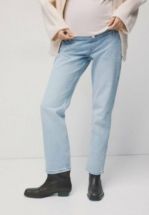 Persoon draagt lichtblauwe rechte jeans, zwarte enkellaarzen en een crèmekleurige trui, en trekt de tailleband iets naar buiten.