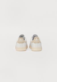 Zapatillas de cuero blancas con detalles de gamuza beige, diseño de punta redonda y suela de goma. Logo "Stan Smith" en el talón en blanco. Estilo minimalista.