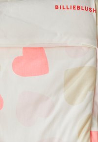 Puuvillane kattekaar, millel on hele kreemivärvi taust, millel on roosa ja beeži südame muster. "BILLIEBLUSH" logo punases värvitoonis peal.