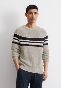 Beige gestrickter Pullover mit weitem Ausschnitt und schwarz-weißen horizontalen Streifen über der Brust. Verfügt über einen strukturierten Stoff und überschnittene Schultern.