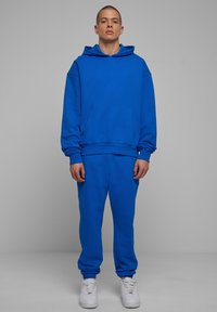 Lys blå hoodie og sæt af sweatpants lavet af blød bomuld. Hoodien har en frontlomme og løs pasform. Sneakers er hvide med perforeringer.