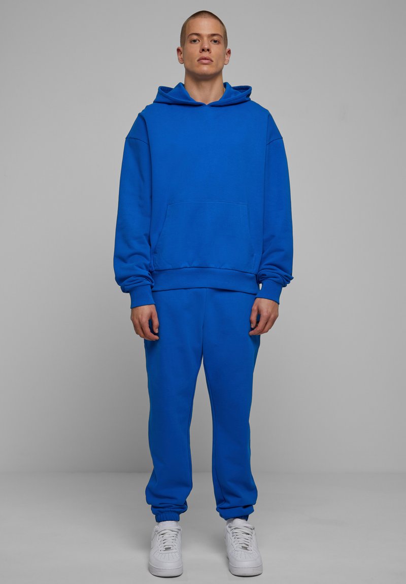 Lys blå hoodie og sæt af sweatpants lavet af blød bomuld. Hoodien har en frontlomme og løs pasform. Sneakers er hvide med perforeringer.