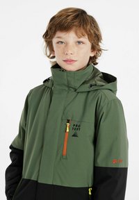 Veste de plein air verte et noire avec une capuche, dotée d'une poche poitrine zippée et d'accents orange. Matériaux imperméables et respirants.
