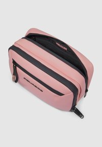 Bolsa de silicona rosa con textura suave, con una cremallera y un logo negros que contrastan. Compartimentos divididos para almacenamiento organizado.