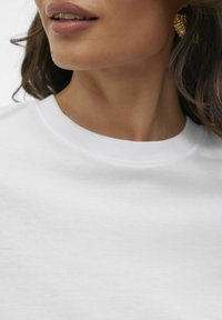 Sweatshirt en coton blanc avec un col rond et une texture lisse, présentant un gros plan sur le col et la peau en dessous.