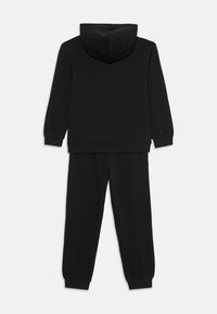 Sweatshirt à capuche noire avec des manches longues et un pantalon de jogging noir assorti, tous deux avec des ourlets côtelés, montrés de dos sur un fond blanc.