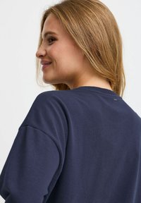 Sudadera azul marino hecha de algodón suave, con cuello redondo, mangas largas y un diseño minimalista que incluye una pequeña etiqueta de marca en la parte posterior.