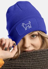 Blue knitted beanie with a patch featuring a white dog silhouette. The ribbed texture adds detail, and the fit appears snug.