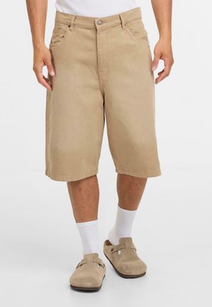 Pantaloni corti in cotone beige con taglio dritto, due tasche frontali e chiusura con bottone. Presentano un orlo che termina appena sopra il ginocchio.