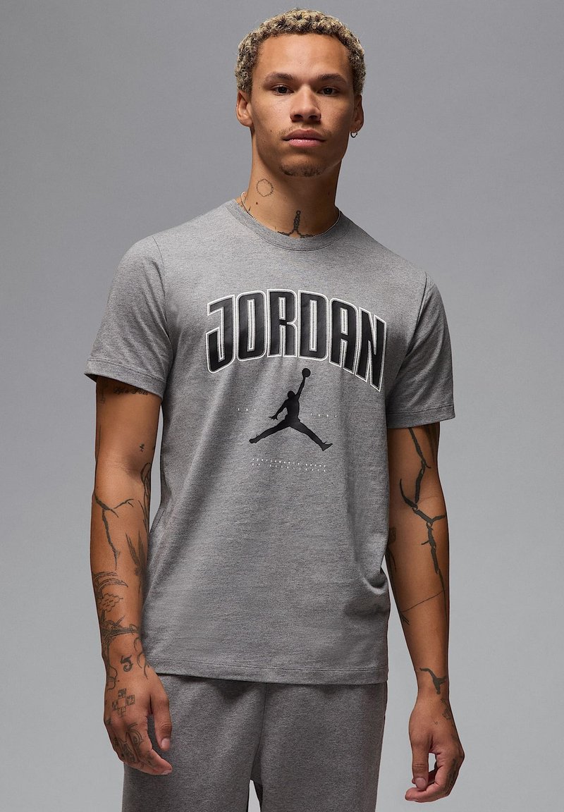 T-shirt in cotone grigio con la scritta "JORDAN" in grassetto nero, un logo silhouette nero e dettagli grafici delicati sottostanti.